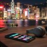 A smartphone with audio waves sits beside headphones, with Hong Kong lights blurred behind it.
