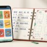A smartphone with colorful language flashcards beside an open Mandarin study notebook.