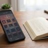 A smartphone showing a Japanese reading app beside an open book on a warm desk.
