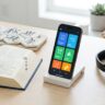 Smartphone beside a dictionary, character tiles, and headphones on a bright desk.