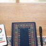 A phone with a language lesson sits beside a notebook, pen, and earbuds.