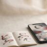 A smartphone and Korean study notebook sit on a desk with wooden tools.