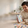 Adult using a smartphone at a bright desk with headphones, coffee, and colorful tokens.
