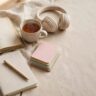 A language workbook, tea, headphones, and flashcards beside a fresh notebook and pen.