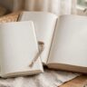 An open reader and thicker novel sit beside a cup of tea.
